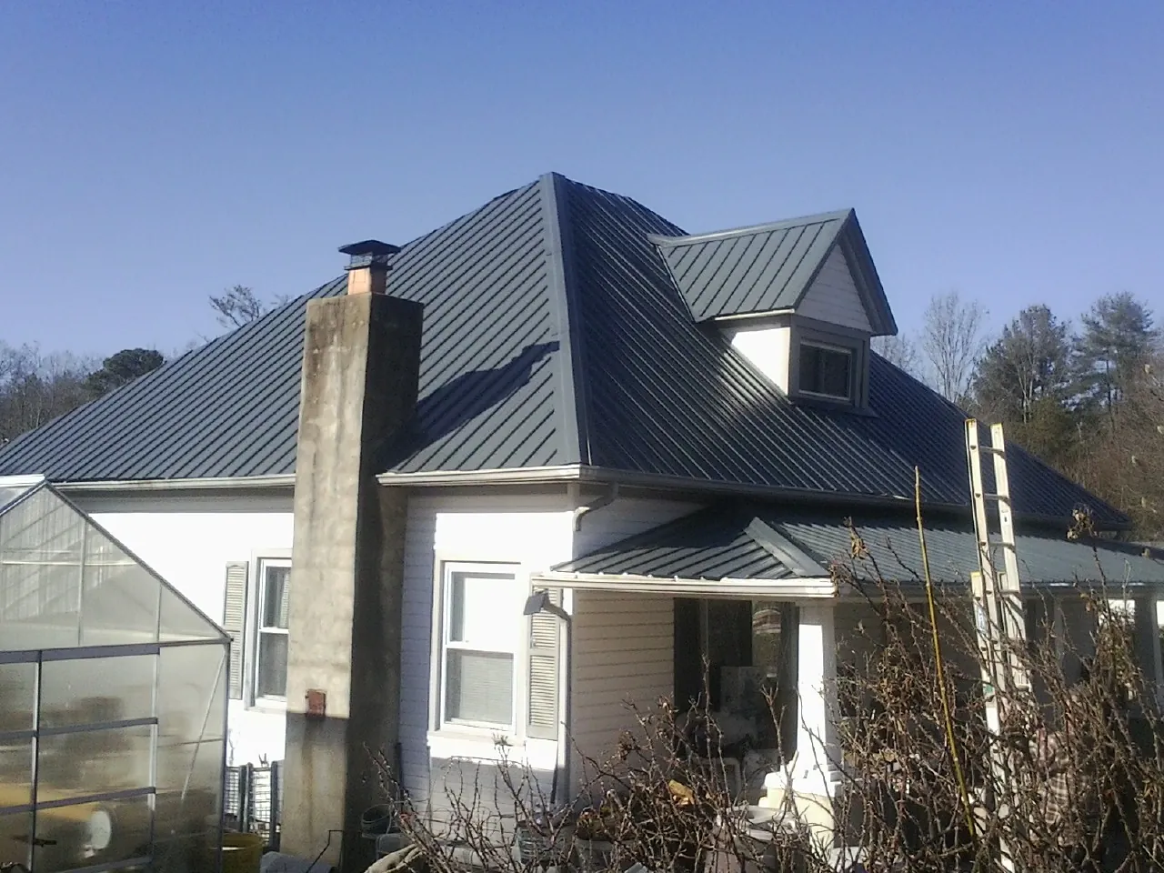 Dark blue standing seam metal roof on a white farmhouse with dormer — Slate & Tile Roof Repair by Roofing Brothers in Pardeeville