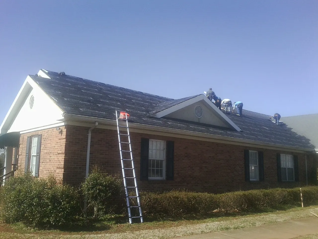 Crew tearing shingles off a brick ranch roof with a ladder set — Emergency Roof Repair work by our crew in Pardeeville