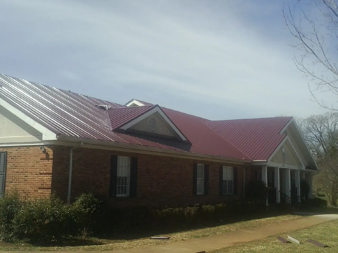 Red metal roof with gabled entries on a long brick building, from a Hail Damage Roof Repair job in Pardeeville