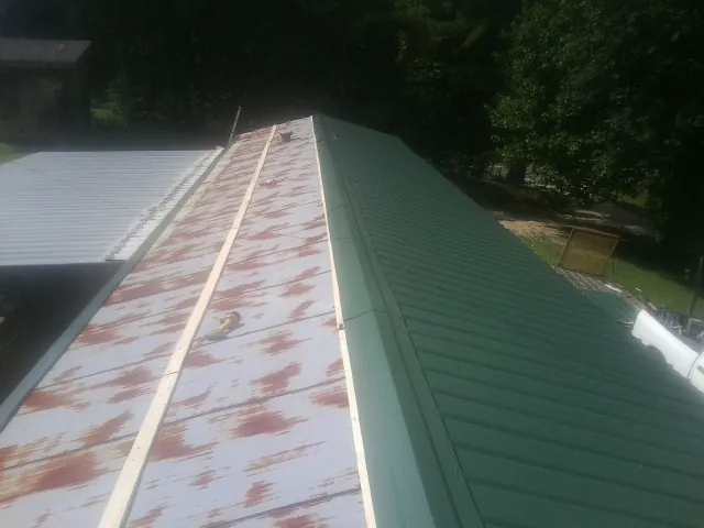 Old rusted panels beside newly installed green metal roofing — Wind Damage Roof Repair by Roofing Brothers in Pardeeville