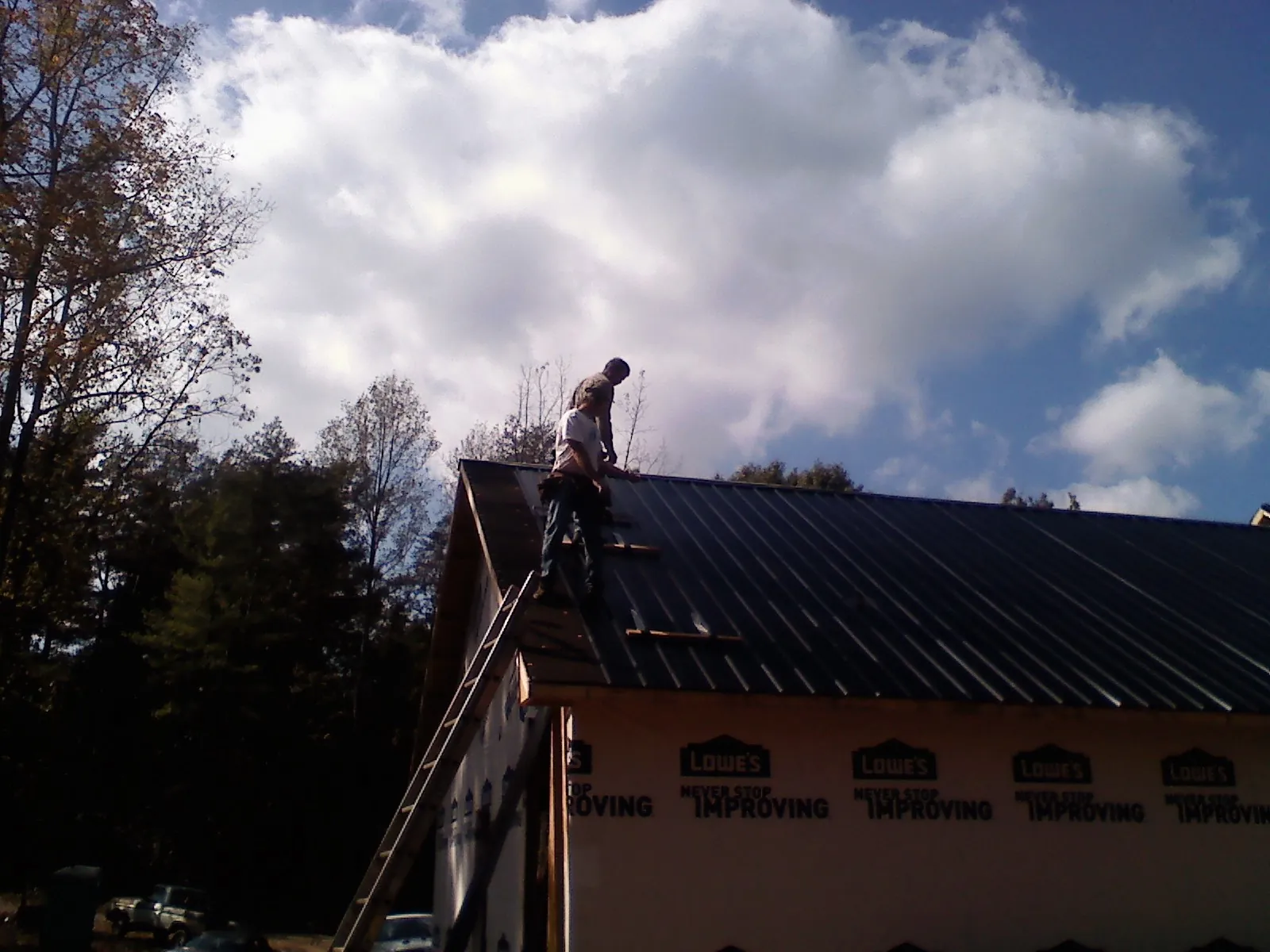 Roofer fastening dark metal panels high against a cloudy sky, from a Roof Inspection job in Pardeeville